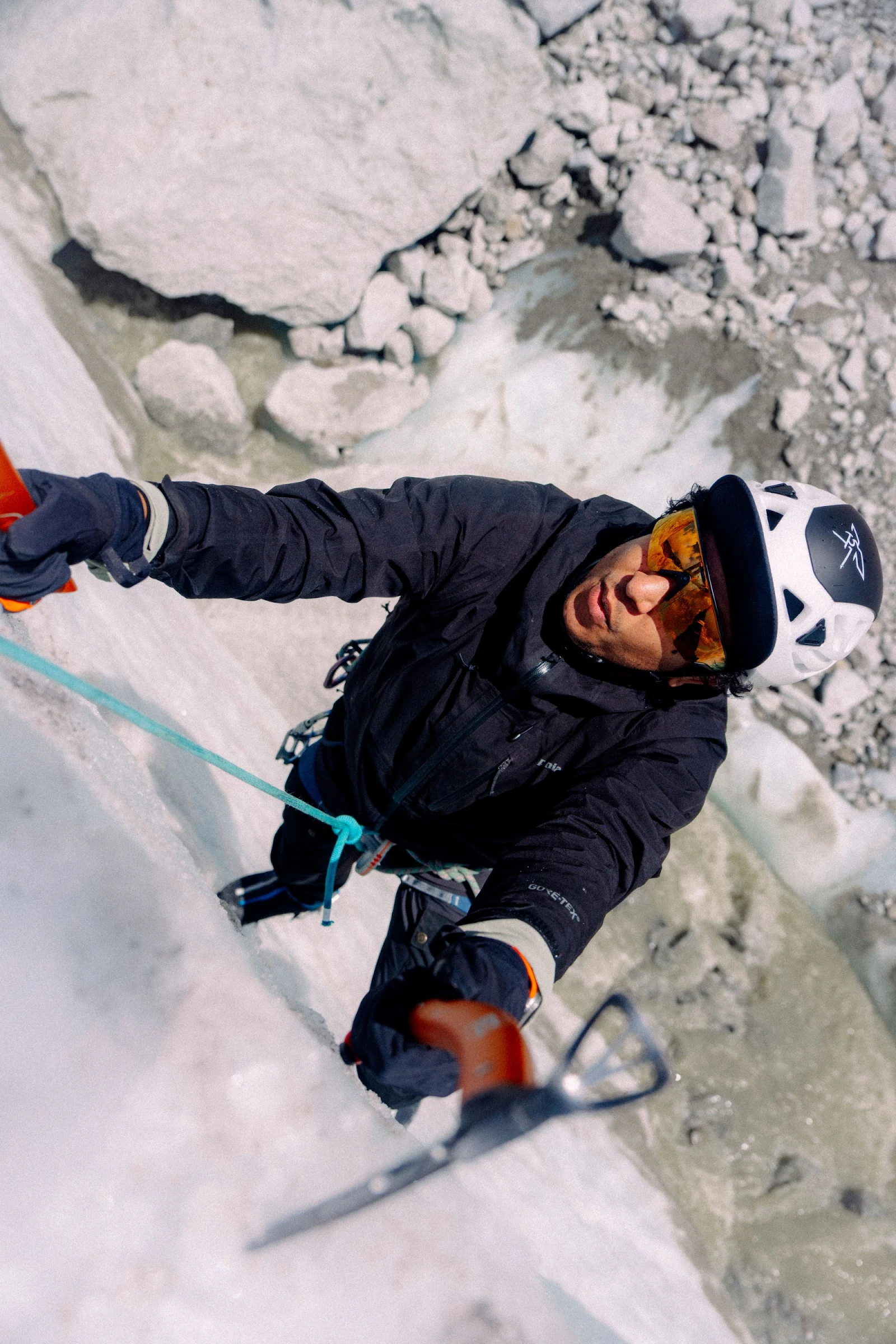 Pedro ice climbing on a glacier while looking up between two ice tools